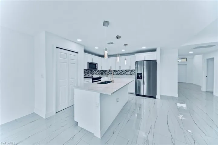 Kitchen with white cabinets, an island with sink, appliances with stainless steel finishes, backsplash, and sink