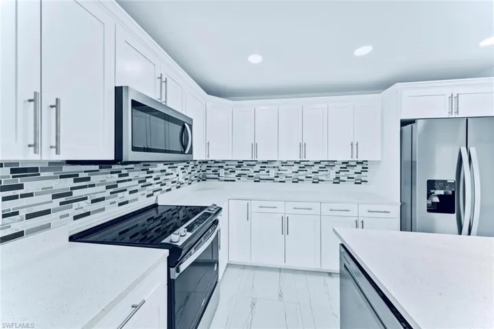 Kitchen with backsplash, appliances with stainless steel finishes, light stone counters, and white cabinets