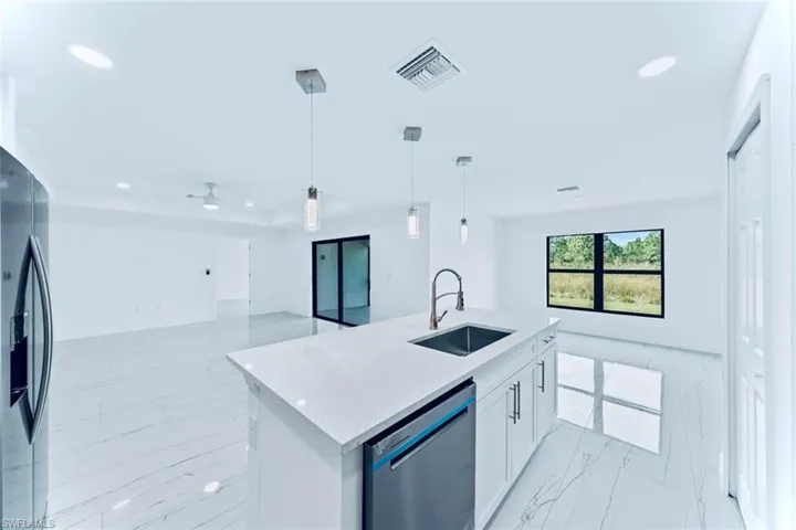 Kitchen featuring a kitchen island with sink, hanging light fixtures, sink, white cabinets, and appliances with stainless steel finishes
