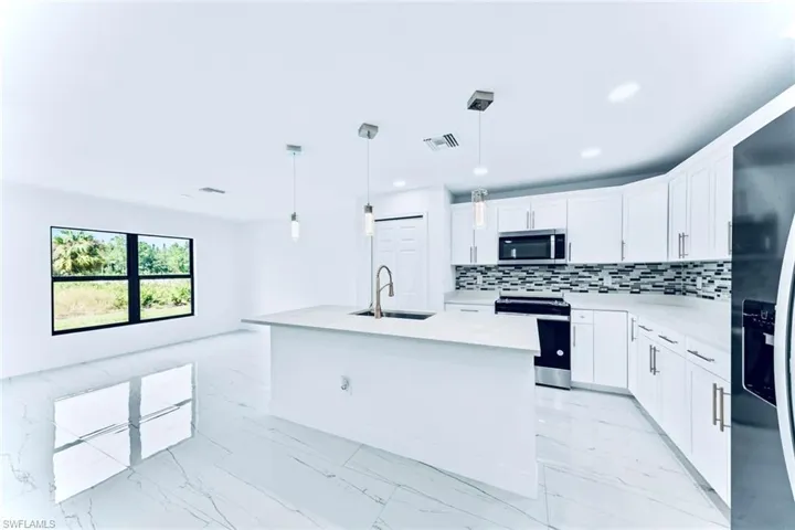 Kitchen with sink, an island with sink, hanging light fixtures, white cabinetry, and stainless steel appliances