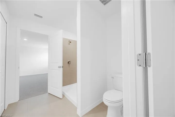 Bathroom featuring a stand-up shower with tiled walls and a white shower pan, a commode, and light-toned tile flooring