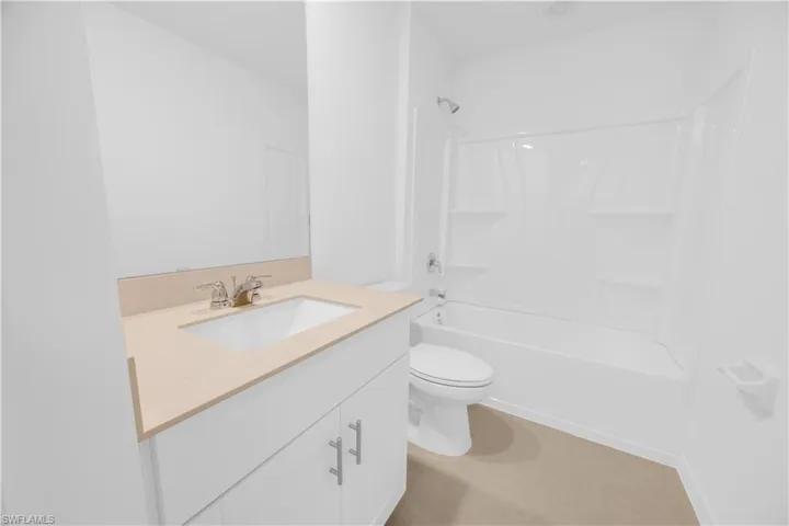 Bathroom featuring a white vanity with brushed nickel hardware, an integrated sink with a chrome faucet, a light-toned countertop, and a white bathtub with a shower combination
