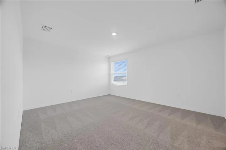 Spacious room featuring light gray carpeting, white walls, a single window with blinds, and a recessed ceiling light