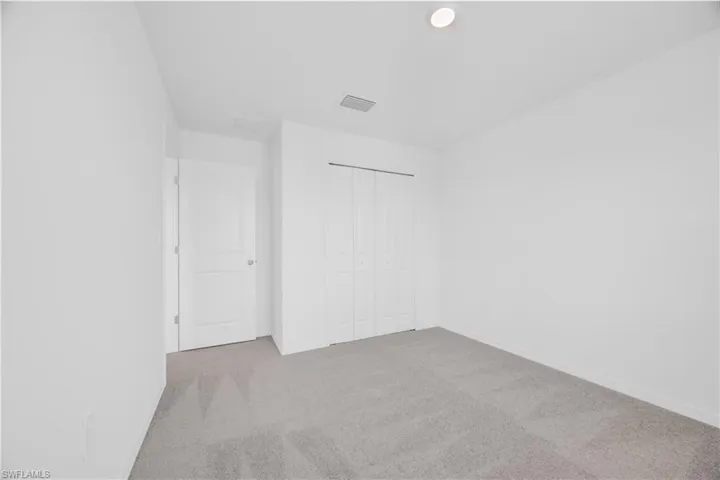 Spacious room with light gray carpeting, crisp white walls, and a recessed ceiling light