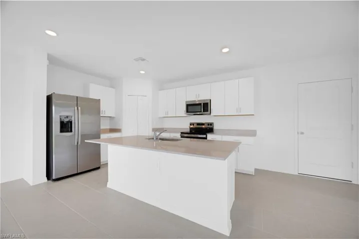 Modern kitchen featuring white cabinetry, light countertops, a large center island with an integrated sink, stainless steel appliances, and recessed lighting