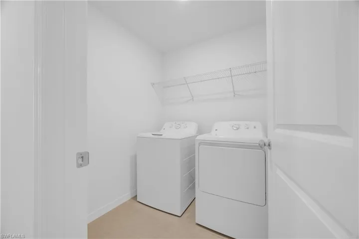 Dedicated laundry area featuring a wire shelf, light-toned flooring, and a crisp white color palette