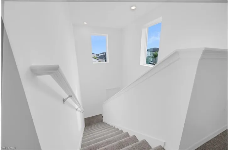 Staircase featuring light gray carpeted steps, white painted walls, white handrail, and two rectangular windows