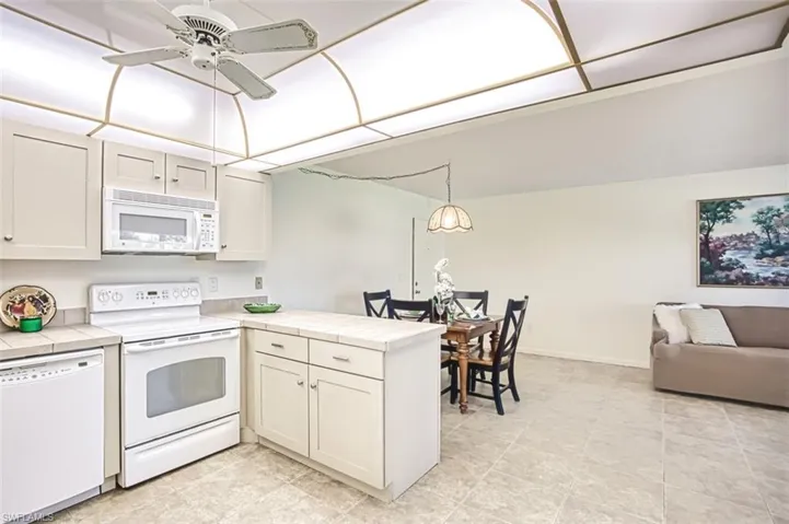 Kitchen with white appliances, open floor plan, a peninsula, tile countertops, and hanging light fixtures