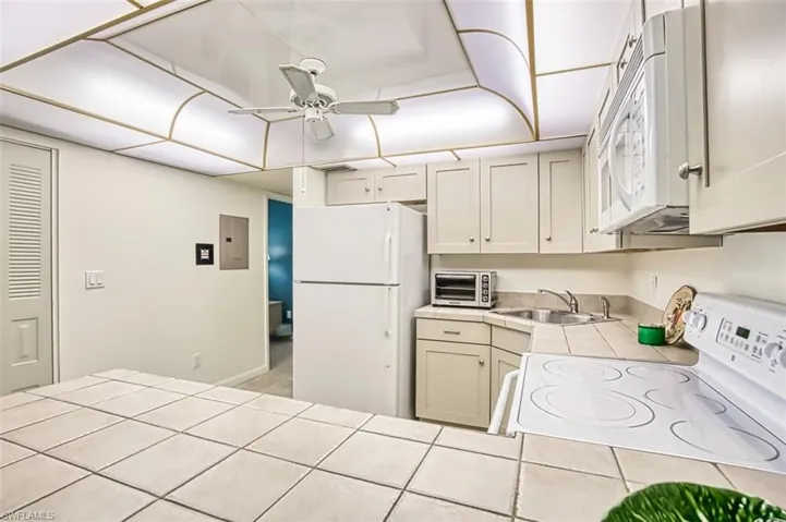 Kitchen featuring tile counters, white appliances, ceiling fan, and electric panel