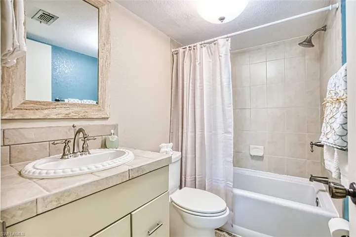 Bathroom featuring shower / bath combo with shower curtain, vanity, and a textured ceiling