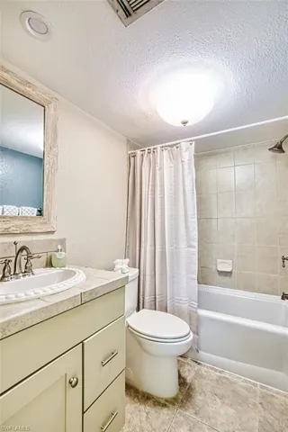 Bathroom featuring shower / bath combination with curtain, vanity, a textured ceiling, and light tile patterned floors