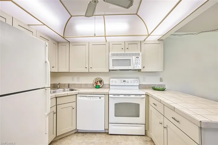 Kitchen featuring white appliances, a peninsula, tile countertops, light tile patterned floors, and a ceiling fan