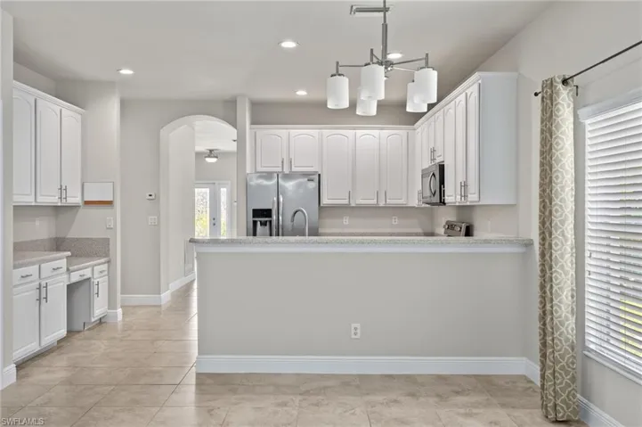 Kitchen with kitchen peninsula, stainless steel appliances, pendant lighting, light tile floors, and white cabinetry