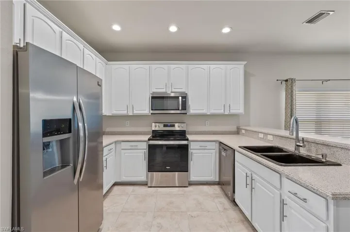 Kitchen featuring kitchen peninsula, light tile floors, sink, white cabinetry, and appliances with stainless steel finishes