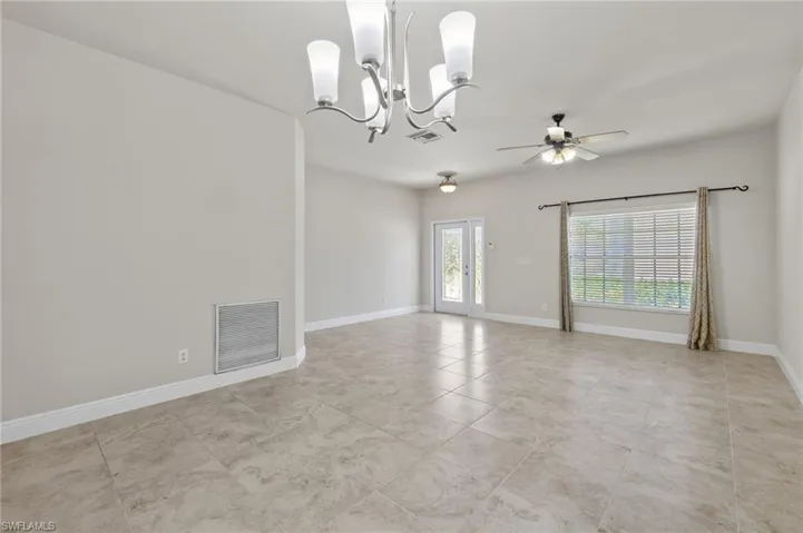 Spare room featuring french doors, light tile flooring, and ceiling fan with notable chandelier