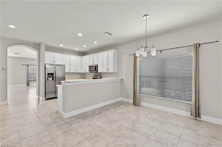 Kitchen featuring light tile flooring, kitchen peninsula, stainless steel appliances, hanging light fixtures, and white cabinets