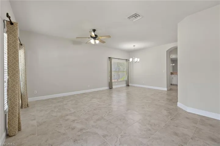 Empty room featuring light tile floors and ceiling fan with notable chandelier