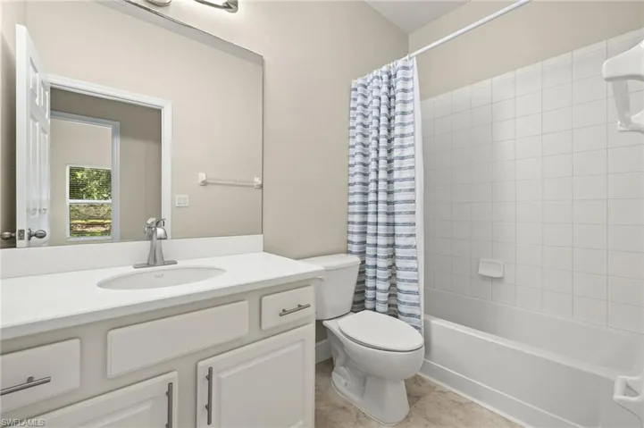 Full bathroom with vanity with extensive cabinet space, shower / bath combination with curtain, tile flooring, and toilet