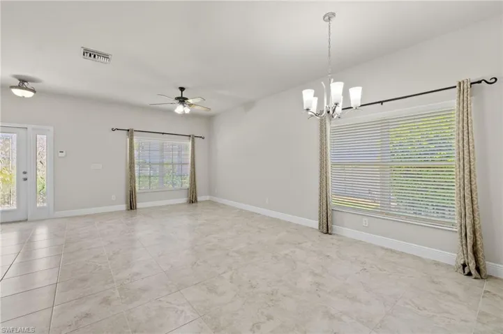 Tiled spare room featuring ceiling fan with notable chandelier