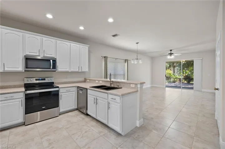 Kitchen with stainless steel appliances, kitchen peninsula, decorative light fixtures, sink, and light tile floors