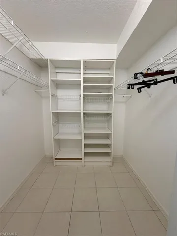 Walk-in closet featuring built-in white shelving, wire shelving, hanging rods, and tile flooring
