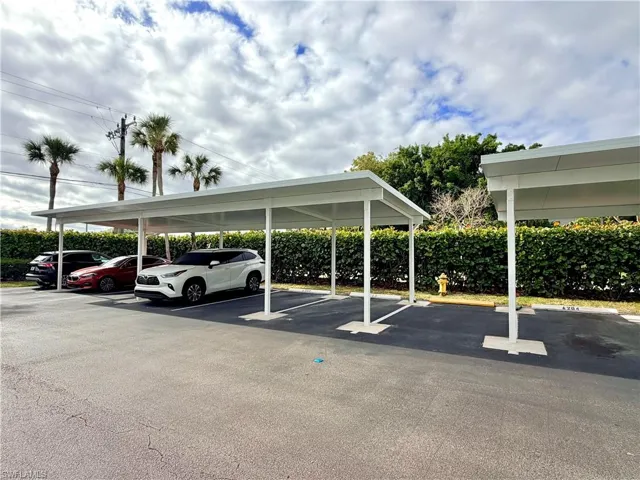 Covered parking structure featuring multiple parking spaces, asphalt paving, and a surrounding hedge row