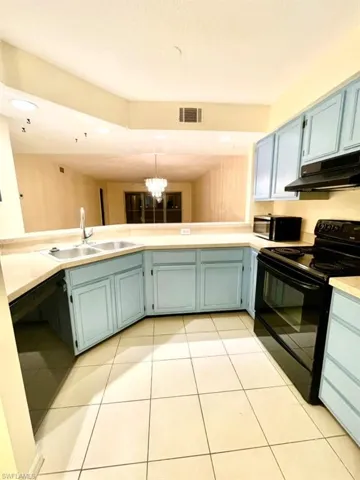 Kitchen with black appliances, a chandelier, light countertops, under cabinet range hood, and light tile patterned floors