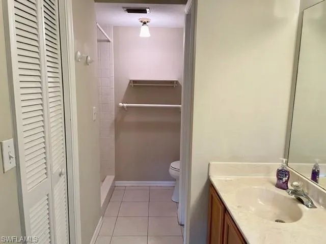 Full bath with light tile patterned flooring, toilet,  closet and a tile shower