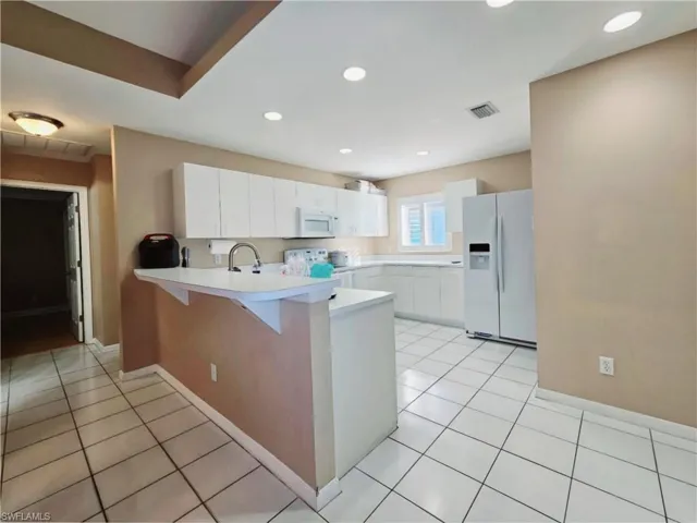 Kitchen with white appliances, a kitchen breakfast bar, kitchen peninsula, light tile patterned flooring, and white cabinetry