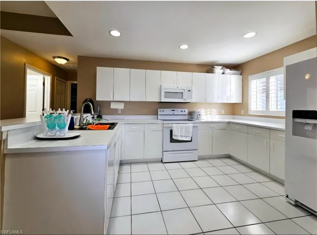 Kitchen with kitchen peninsula, white appliances, sink, white cabinets, and light tile patterned flooring