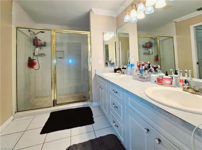 Master Bathroom with tile patterned floors, vanity, ornamental molding, and a shower with door
