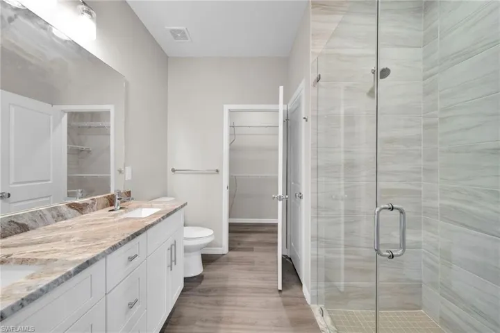 Bathroom featuring hardwood / wood-style floors, walk in shower, double vanity, and toilet