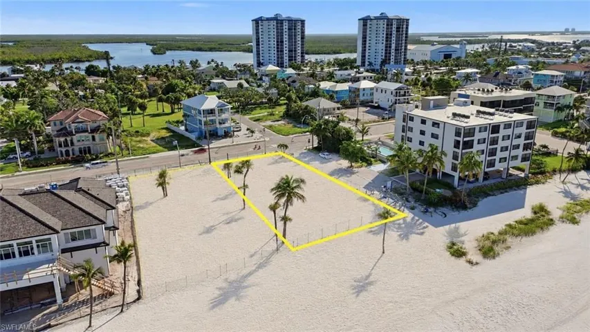 Expansive sandy lot with several palm trees directly on a beach, featuring a clear water body in the background - Virtually Edited Image
