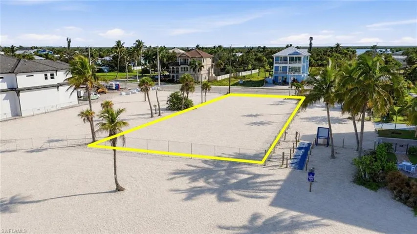 Expansive sandy lot with a perimeter fence, mature palm trees, and a clear, flat building area - Virtually Edited Image