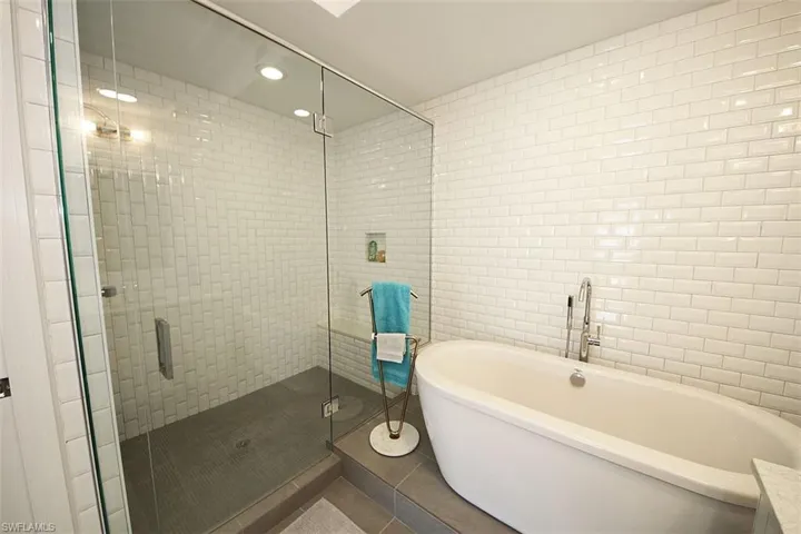 Full bath with tile walls, a stall shower, tile patterned floors, a freestanding bath, and recessed lighting
