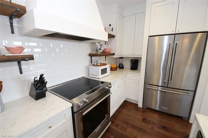 Kitchen featuring open shelves, custom exhaust hood, stainless steel appliances, decorative backsplash, and white cabinetry