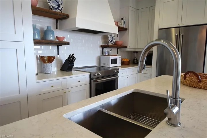Kitchen featuring open shelves, backsplash, premium range hood, light stone counters, and stainless steel appliances