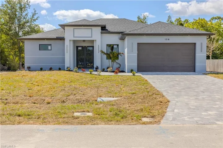 Prairie-style house with stucco siding, french doors, decorative driveway, a front yard, and a garage