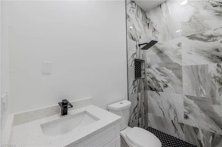 Bathroom with a marble finish shower, toilet, and vanity