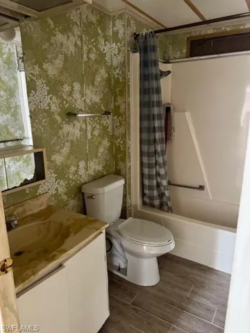 Full bath featuring wallpapered walls, vanity, shower / bath combo, and wood finished floors