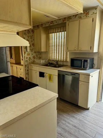 Kitchen with appliances with stainless steel finishes, custom range hood, light wood finished floors, light countertops, and wallpapered walls