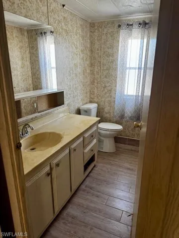 Bathroom featuring crown molding, wallpapered walls, wood finished floors, and vanity