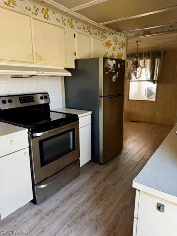 Kitchen featuring appliances with stainless steel finishes, light wood finished floors, light countertops, tasteful backsplash, and wallpapered walls