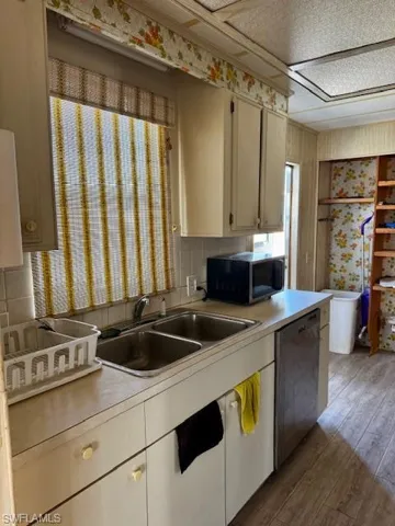 Kitchen featuring stainless steel dishwasher, light countertops, wood finished floors, and tasteful backsplash