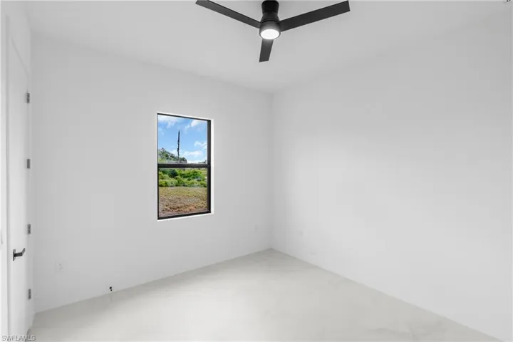 Bright interior space featuring a window with a natural landscape, a contemporary ceiling fan with integrated lighting, a white painted door with a black lever handle, and light-toned tile flooring