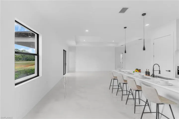 Open-concept living area with large format tile flooring, a kitchen island with integrated sink and matte black faucet, pendant lighting, and a window with black trim