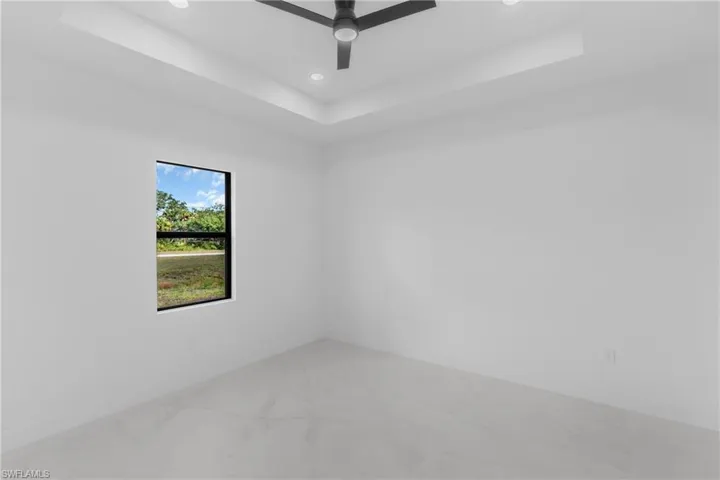 Spacious room featuring a tray ceiling with recessed lighting, a contemporary ceiling fan, a large window with black trim, and light-toned tile flooring