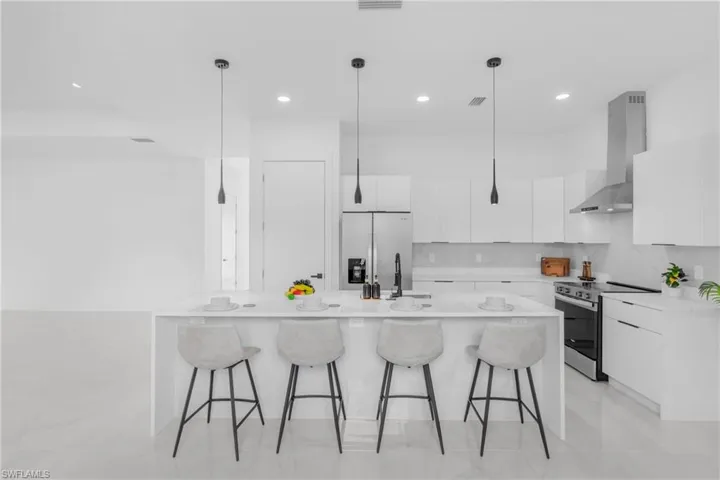 Modern kitchen featuring a waterfall island, stainless steel appliances, white cabinetry, and recessed lighting
