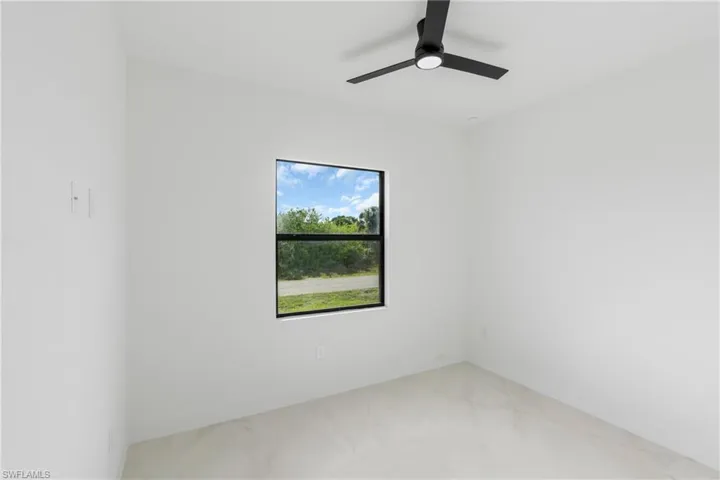 Bright interior space featuring a window with a black frame, a ceiling fan with integrated lighting, and light-toned flooring