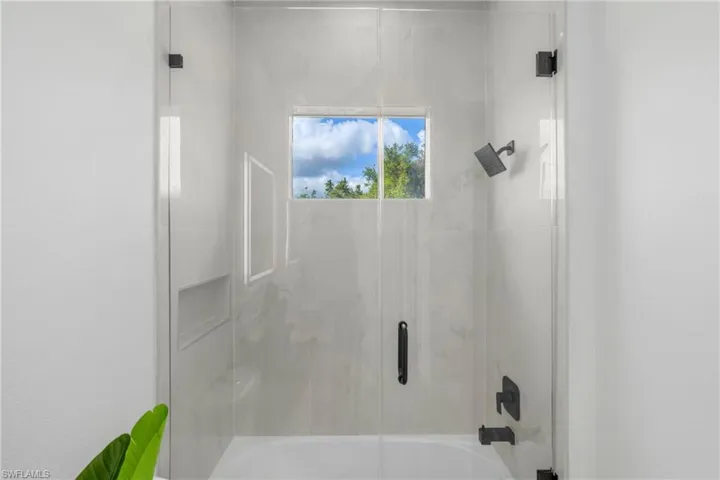 Bathtub and shower combination featuring a glass enclosure, matte black fixtures, an inset shower niche, and a rectangular window